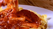 Wrapping ribbon pasta with tomato sauce and prawns round fork