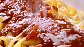Sprinkling Parmesan over ribbon pasta with tomato sauce