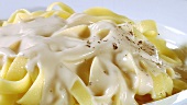 Sprinkling pepper over ribbon pasta with Alfredo sauce