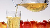 Pouring apple juice out of a jug into a chilled glass