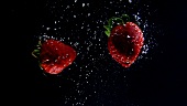 Zwei Erdbeeren schwimmen im Wasser (Schwarzer Hintergrund)