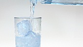 Mineralwasser in ein Glas mit Eiswürfeln gießen