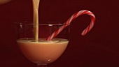 Pouring egg nog into a glass with a candy cane