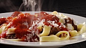 Sprinkling Parmesan over ribbon pasta with meatballs and tomato sauce