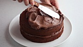 A chocolate cake being spread with chocolate cream