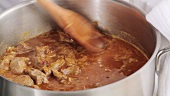 Stirring beef goulash with a wooden spoon