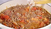 Adding stock to pan of minced meat