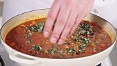 Adding oregano and seasoning to chilli con carne