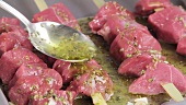Lamb kebabs being drizzled with a herb marinade
