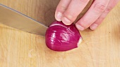 A halved red onion being diced