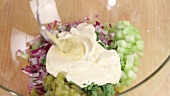 Chopped vegetables being mixed with mayonnaise and mustard