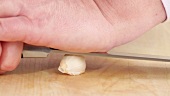 A garlic clove being crushed with the back of a knife and peeled