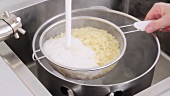 Cooked orzo pasta being poured into a sieve and quenched