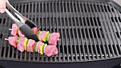 Meat and vegetable kebabs being placed on the grill