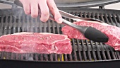 New York strip steaks being placed on a grill