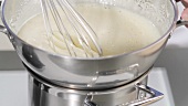 Butter cream in a mixing bowl being placed over a hot bain marie and stirred