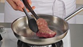 A fillet steak being flipped in a pan
