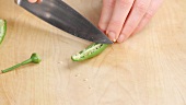 A green chilli pepper being halved and deseeded