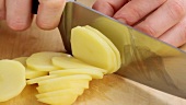 Peeled potato being thinly sliced (close-up)