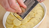 Potato slices in a baking dish being seasoned with nutmeg