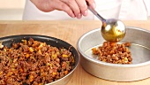 A minced meat and vegetable mixture being placed to a pie tin
