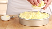 Cottage pie being made: butter and grated cheese being added to a mashed potatoes topping