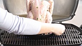 A chicken on a roaster being placed on a barbecue