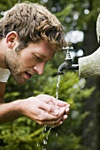 Junger Mann schöpft Wasser am Brunnen