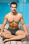 Germany, young man practicing yoga beside swimming pool, portrait