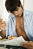 Young man reading newspaper at breakfast