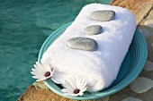 Towel, stones and flowers on plate by swimming pool