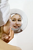 Frau trägt Gesichtsmaske vor dem Spiegel auf
