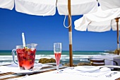 Sangria with berries in jug & sparkling wine glass on table by sea