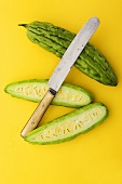 Whole and Halved Bitter Melon with Knife on Yellow Background