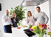 Two couples raising glasses of wine in kitchen