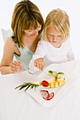 Mother and daughter eating fruit from plate