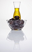 Black olives in glass dish in front of carafe of olive oil