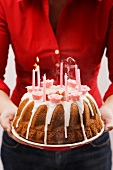 Woman holding iced ring cake with birthday candles