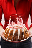 Frau hält Geburtstagsnapfkuchen mit Zuckerguss und Kerzen