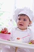 Little girl in chef's hat eating strawberries