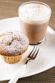 Hot cocoa and muffin with chocolate pieces and icing sugar