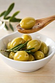 Green olives in small dish and on wooden spoon