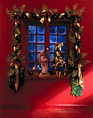 Holly berry leaves garland with golden ribbon around window and angel on window sill
