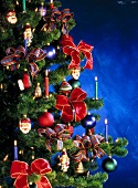 Close-up of Christmas tree with bow, Santa, lit candles and baubles
