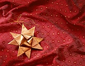 Gefalteter Stern aus Goldpapier, liegt auf rotem, bedrucktem  Tuch