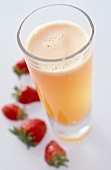 Glas mit Vier-Frucht-Drink neben dem Glas liegen Erdbeeren