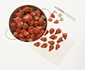 Stahlsieb voller Erdbeeren, davor einige Erdbeeren und ein Messer