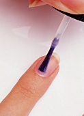 Fingernagel wird mit Schutzlack behandelt