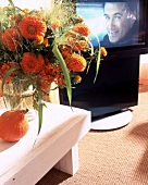 Drehbares TV-Set hinter orangem Blumenstrauss