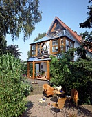 Terrasse mit Korb-Sitzmöbeln v. Haus mit Wintergarten